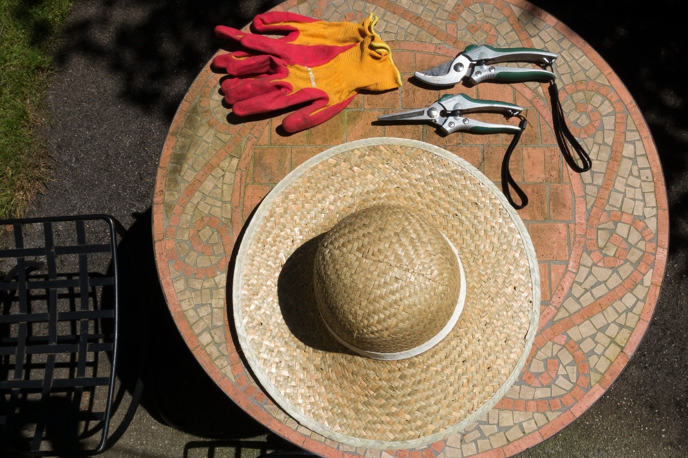 Straw hat, gardening gloves and scissors on mosaic table 